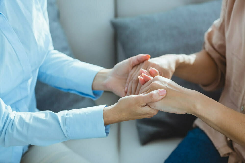 Midsection of therapist holding patient hands on sofa at home