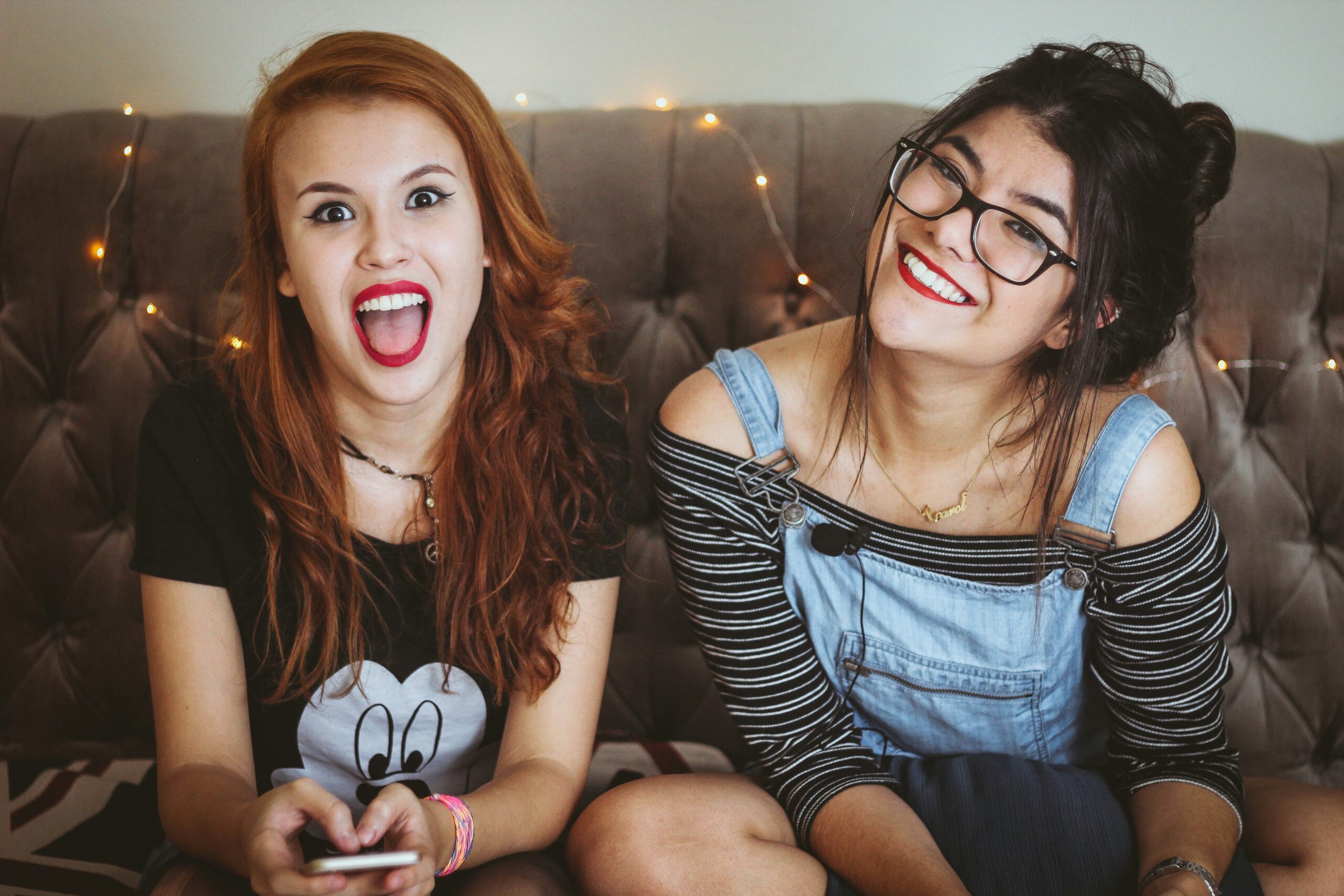Two teen girls having fun, one making a silly face with a phone, the other smiling at her