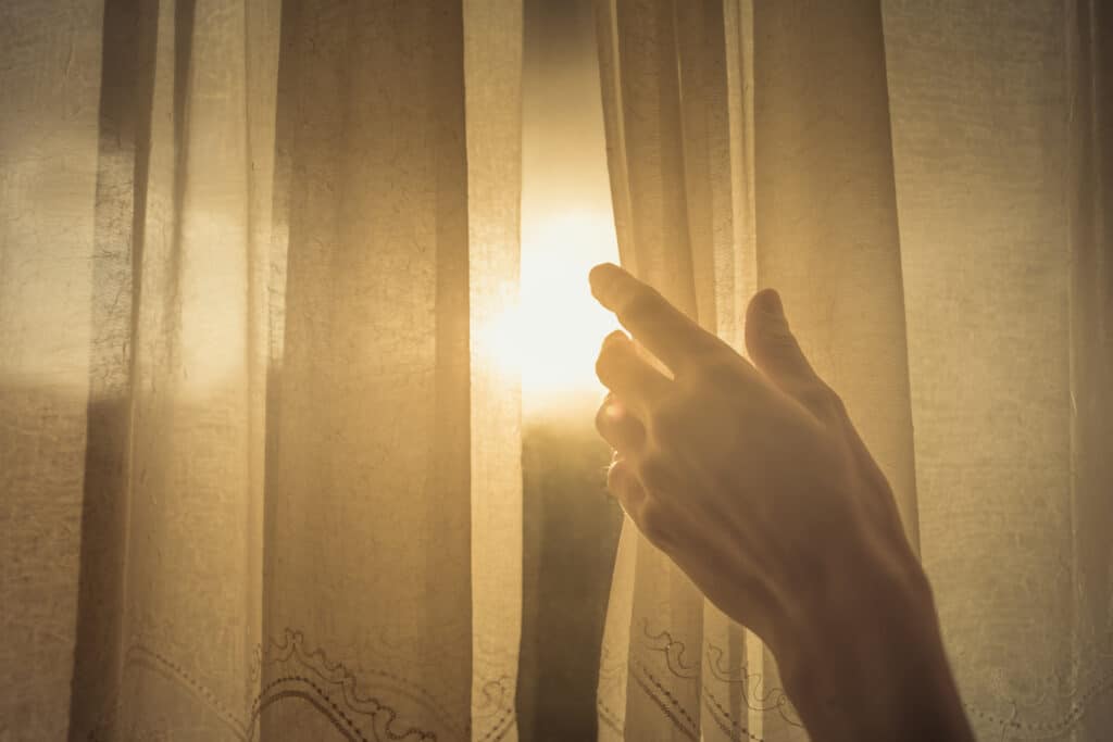 New day and new beginnings, rise and shine concept. Hand opening up window curtain letting the early morning sunshine in. Symbolizing how divorce counselling can help to open the curtains and shine some light on your life.